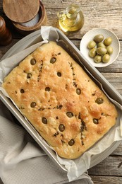 Photo of Delicious focaccia bread with olives, thyme, salt and oil on wooden table, flat lay