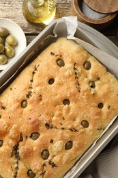 Photo of Delicious focaccia bread with olives, thyme, salt and oil on wooden table, flat lay