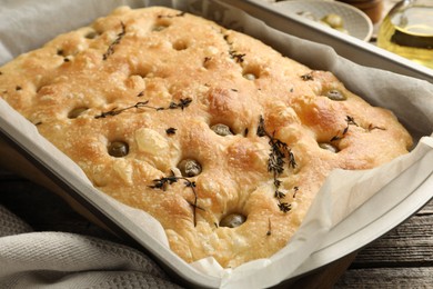 Photo of Delicious focaccia bread with olives and thyme on wooden table, closeup