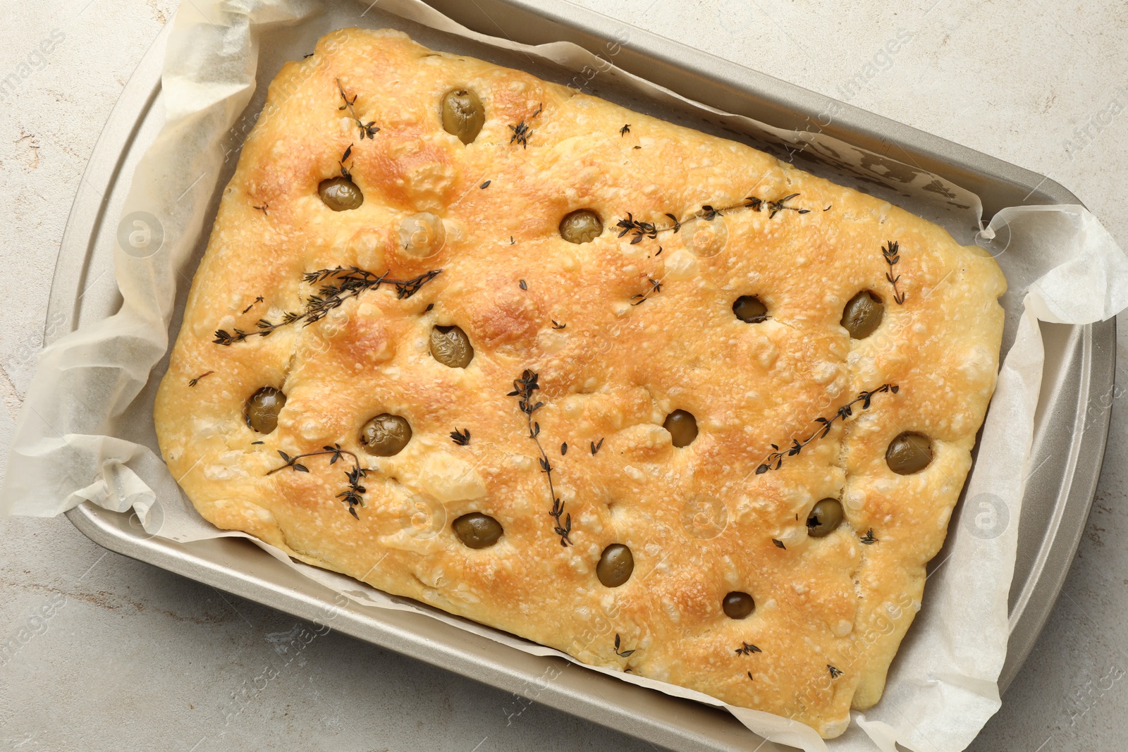 Photo of Delicious focaccia bread with olives and thyme in baking dish on light grey table, top view