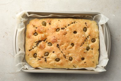 Photo of Delicious focaccia bread with olives and thyme in baking dish on light grey table, top view