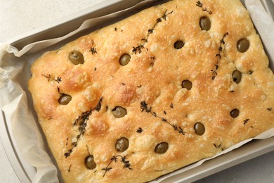 Photo of Delicious focaccia bread with olives and thyme in baking dish on light grey table, top view