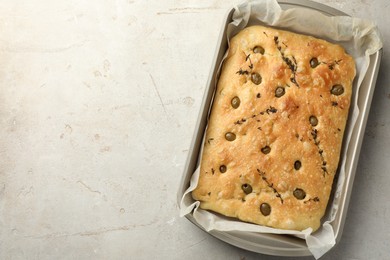 Photo of Delicious focaccia bread with olives and thyme in baking dish on light grey table, top view. Space for text