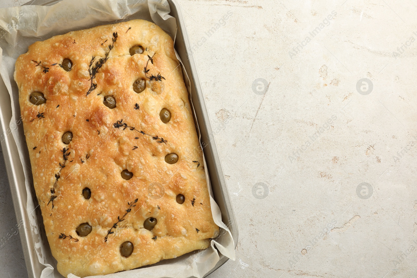 Photo of Delicious focaccia bread with olives and thyme in baking dish on light grey table, top view. Space for text