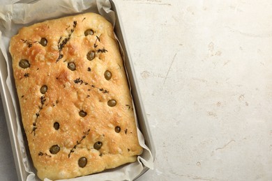 Photo of Delicious focaccia bread with olives and thyme in baking dish on light grey table, top view. Space for text