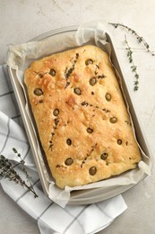 Photo of Delicious focaccia bread with olives and thyme in baking dish on light grey table, top view