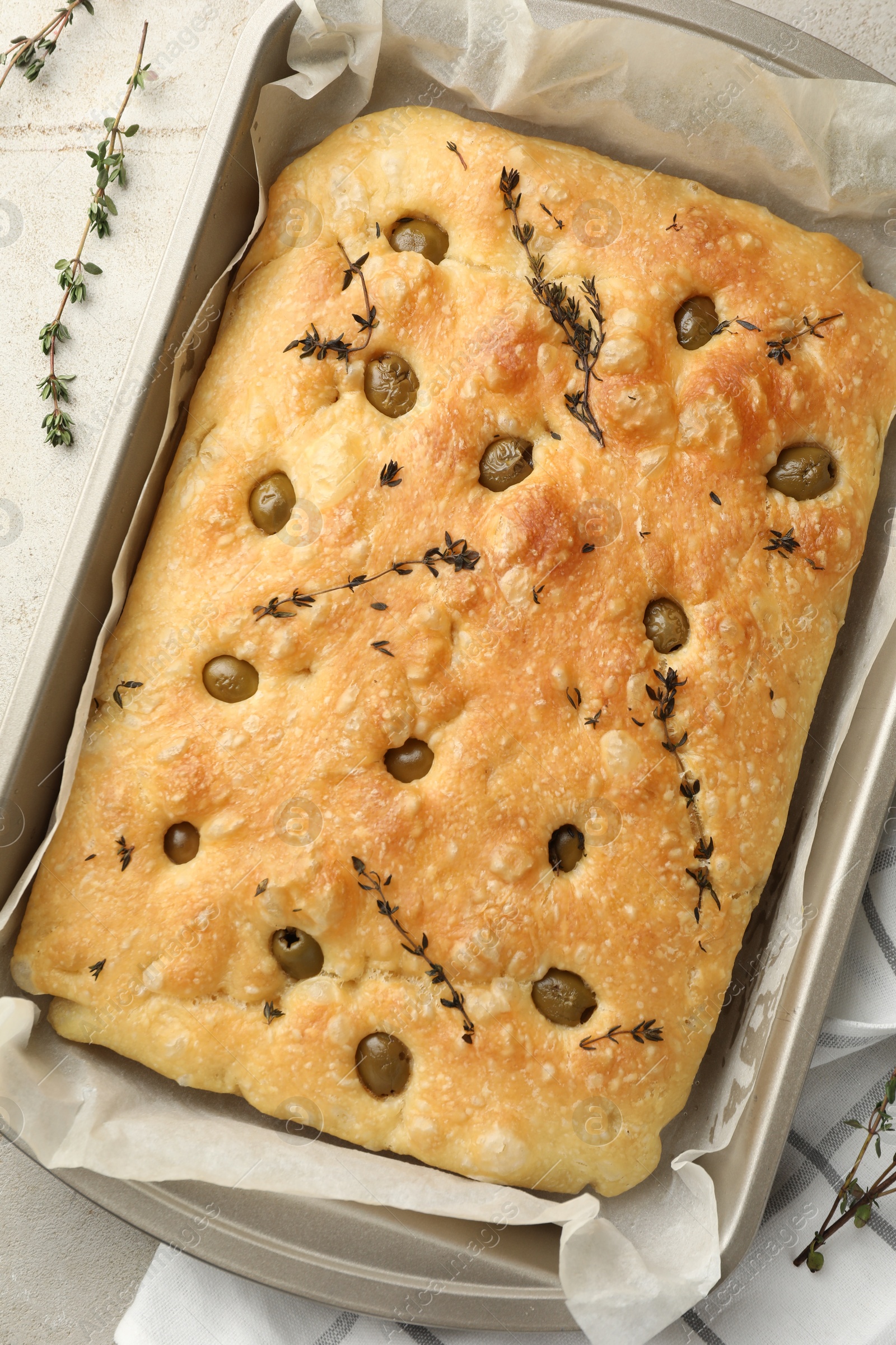 Photo of Delicious focaccia bread with olives and thyme in baking dish on light grey table, top view