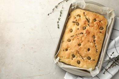 Photo of Delicious focaccia bread with olives and thyme in baking dish on light grey table, top view. Space for text