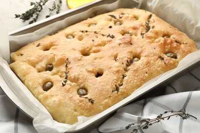 Photo of Delicious focaccia bread with olives and thyme in baking dish on table, closeup