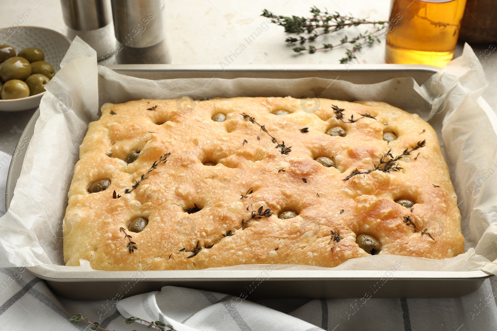 Photo of Delicious focaccia bread with olives, thyme and oil in baking dish on light grey table, closeup