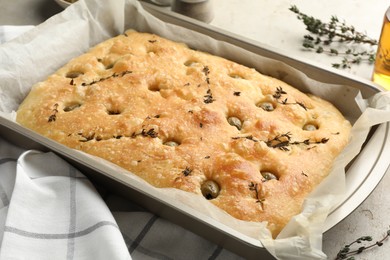 Photo of Delicious focaccia bread with olives and thyme in baking dish on table, closeup