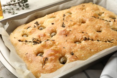 Photo of Delicious focaccia bread with olives and thyme in baking dish on table, closeup