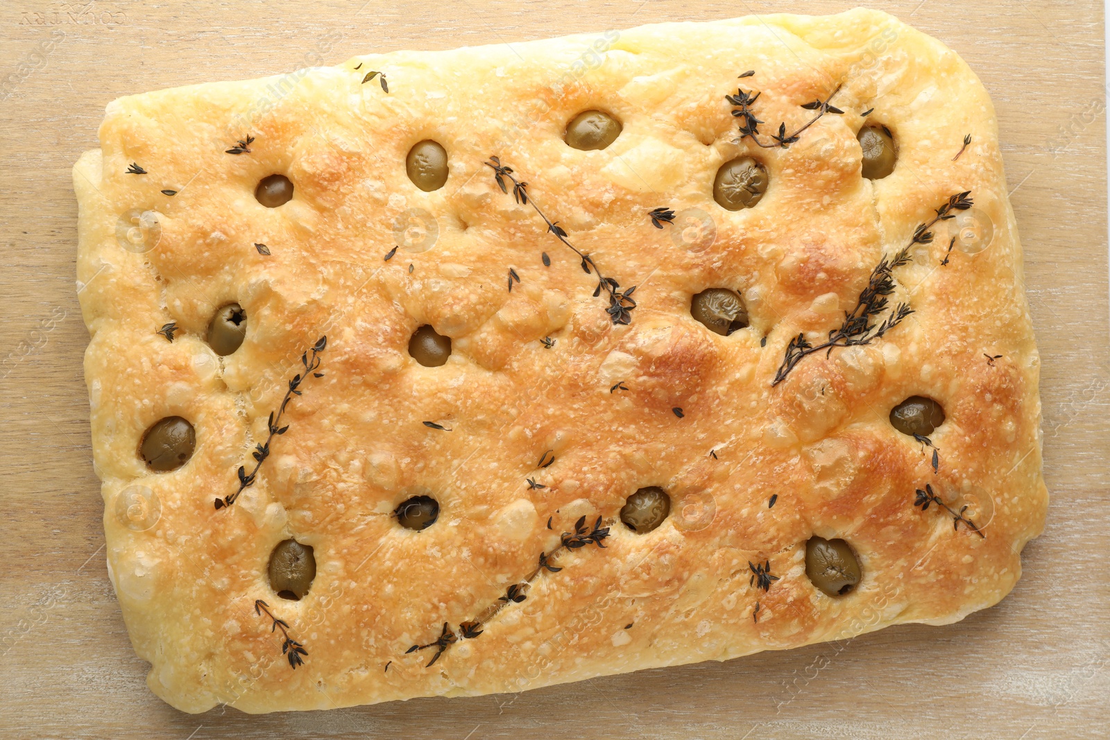 Photo of Delicious focaccia bread with olives and thyme on wooden table, top view