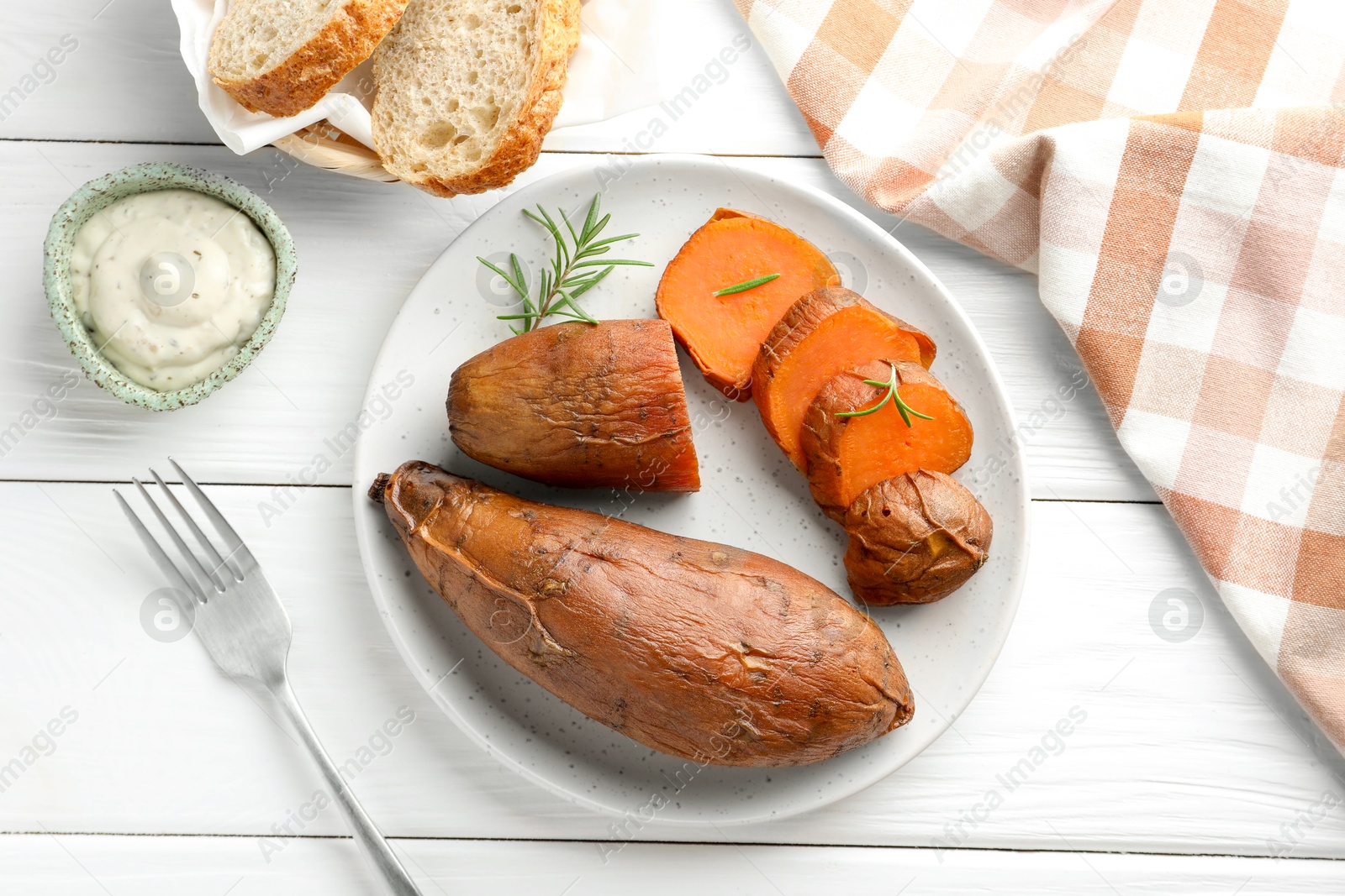 Photo of Tasty cooked sweet potatoes served with rosemary and sauce on white wooden table, top view