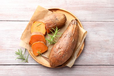 Photo of Tasty cooked sweet potatoes and rosemary on wooden table, top view