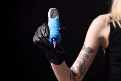 Photo of Professional artist in gloves holding tattoo machine on black background, closeup. Space for text