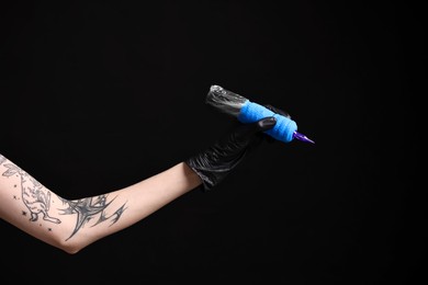 Photo of Professional artist in gloves holding tattoo machine on black background, closeup. Space for text