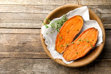 Photo of Halves of tasty cooked sweet potato with thyme on wooden table, top view. Space for text