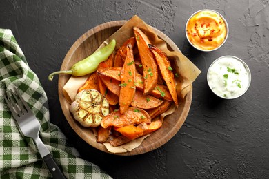 Photo of Tasty cooked sweet potatoes with garlic, pickled pepper and sauces on black table, top view