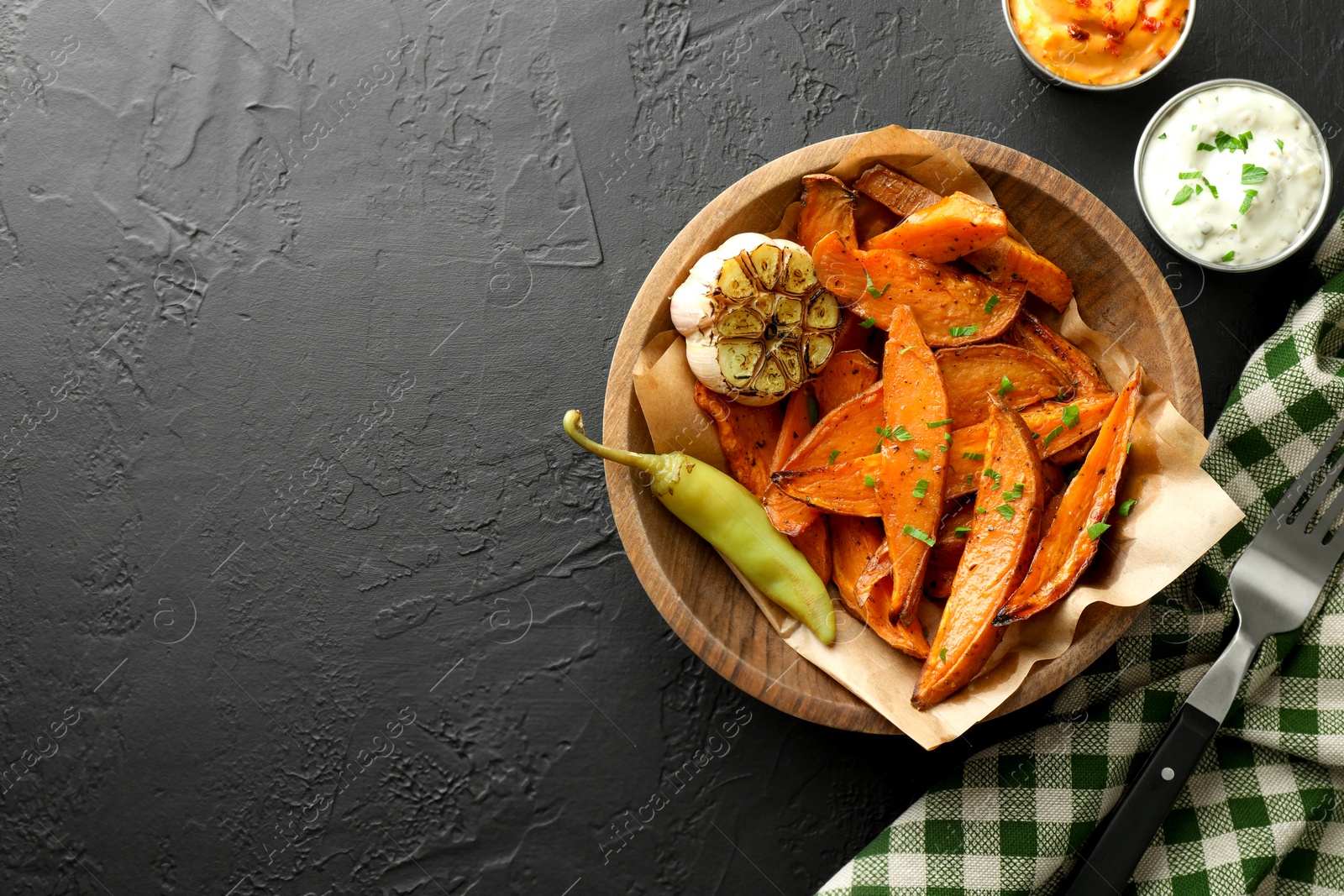 Photo of Tasty cooked sweet potatoes with garlic, pickled pepper and sauces on black table, top view. Space for text