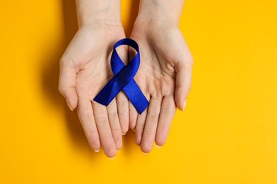 Photo of Woman with dark blue ribbon on yellow background, top view. Arthritis disease and colon cancer awareness