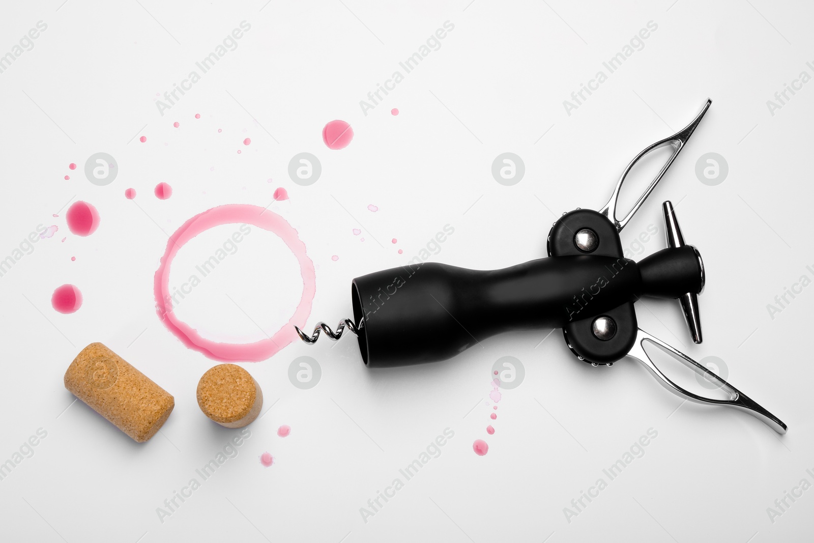 Photo of Wing corkscrew, corks and red wine stains on white background, top view