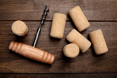 Corkscrew and corks on wooden table, flat lay