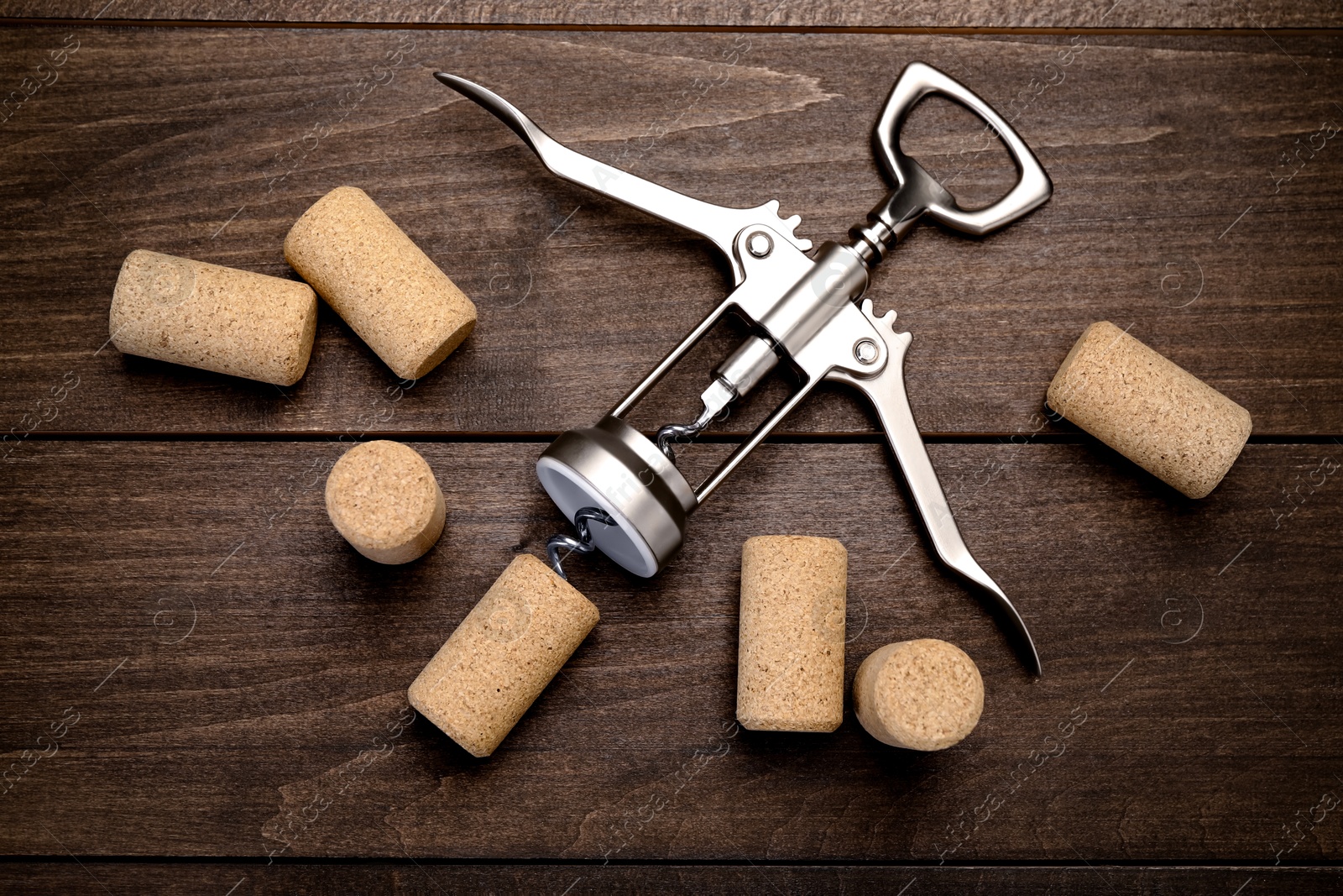 Photo of Wing corkscrew and corks on wooden table, flat lay