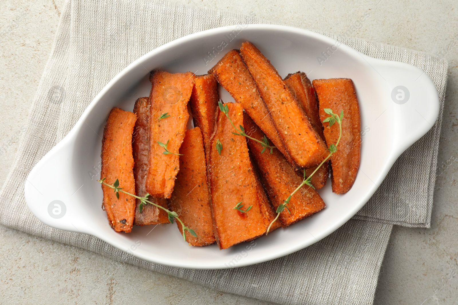 Photo of Pieces of tasty cooked sweet potato with microgreens in baking dish on light textured table, top view