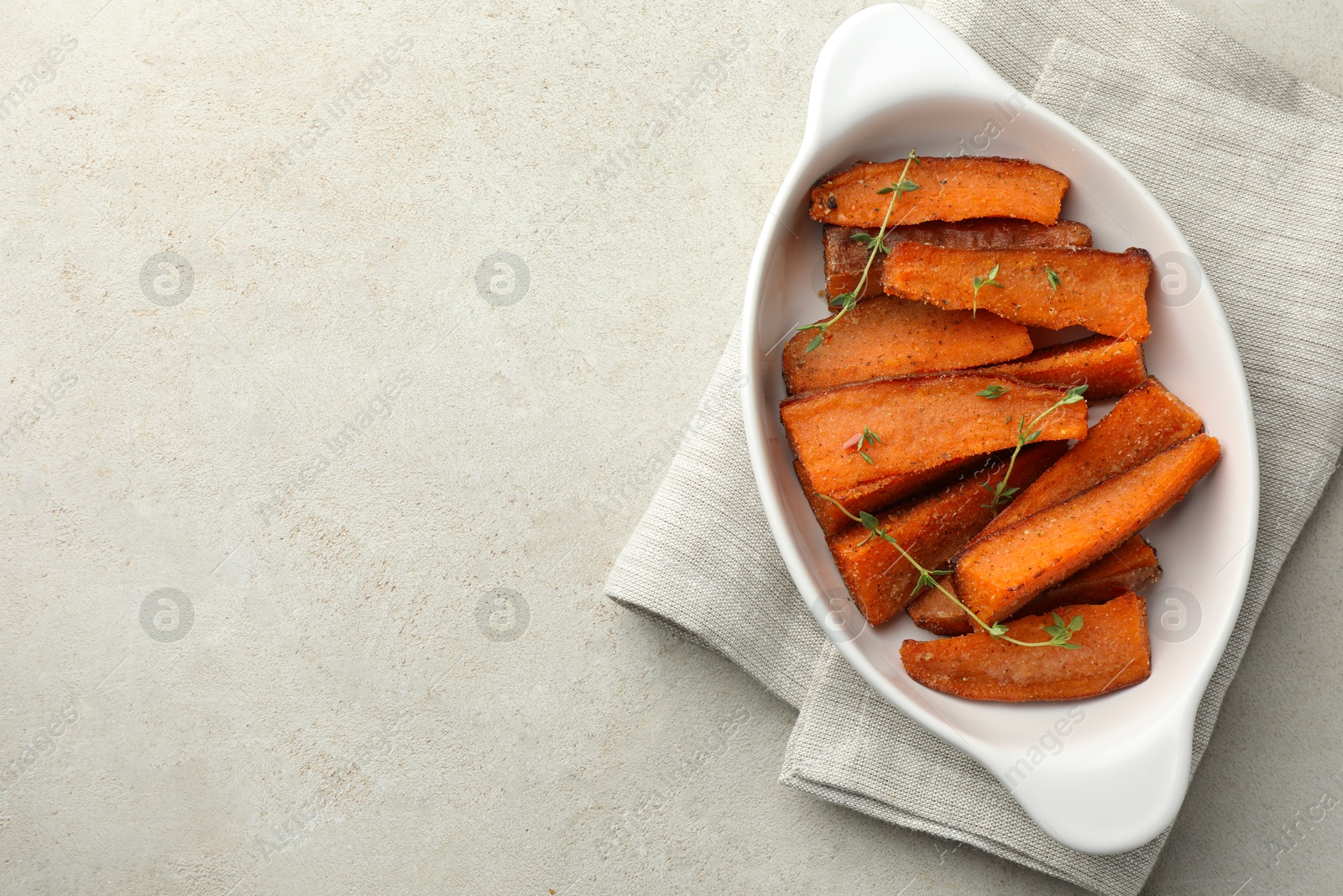 Photo of Pieces of tasty cooked sweet potato with microgreens in baking dish on light textured table, top view. Space for text