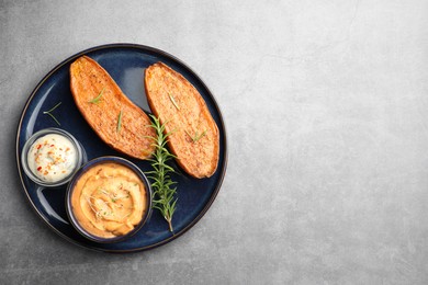 Photo of Halves of tasty baked sweet potato served with sauces on grey textured table, top view. Space for text