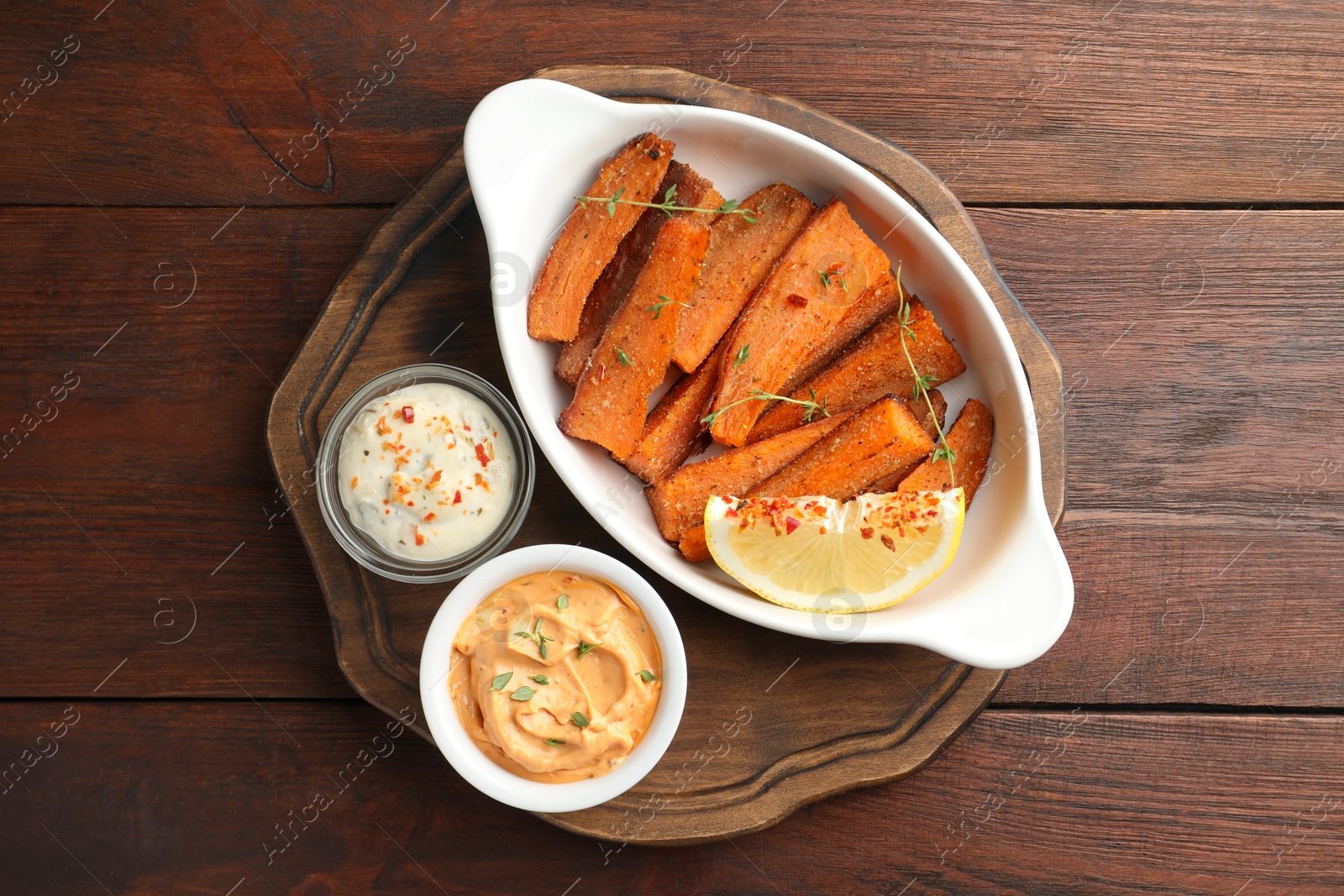 Photo of Pieces of tasty cooked sweet potato in baking dish served on wooden table, top view