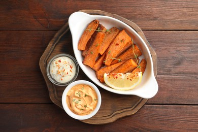 Photo of Pieces of tasty cooked sweet potato in baking dish served on wooden table, top view