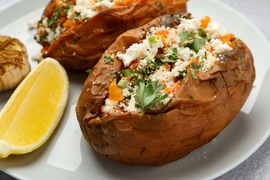 Photo of Tasty baked sweet potatoes with feta cheese, parsley and lemon slice on table, closeup