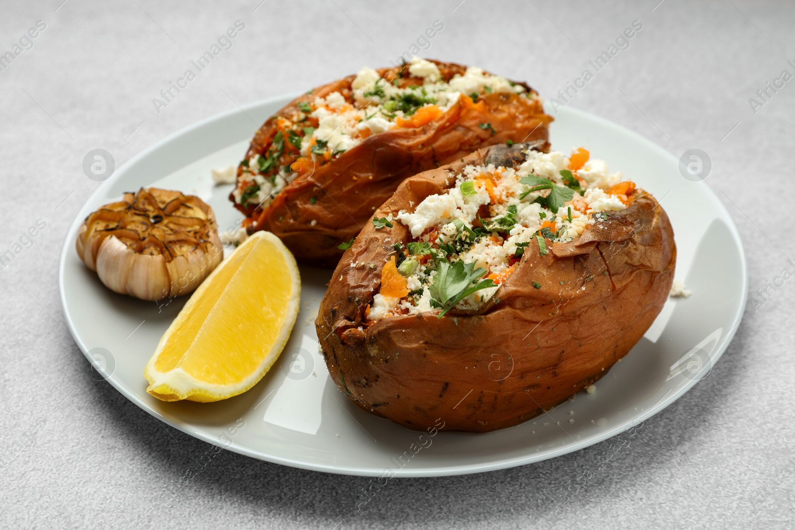 Photo of Tasty baked sweet potatoes with feta cheese, parsley and lemon slice on light textured table, closeup