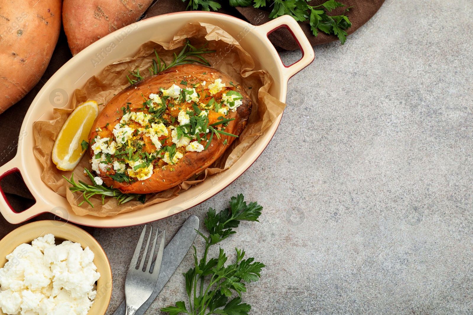 Photo of Tasty baked sweet potato with feta cheese and herbs on grey textured table, flat lay. Space for text