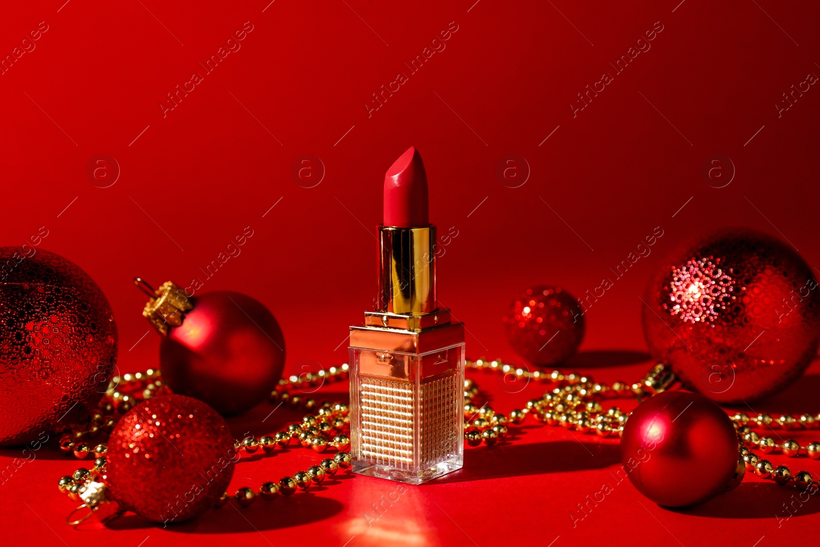 Photo of Christmas gift. Lipstick and festive decor on red background