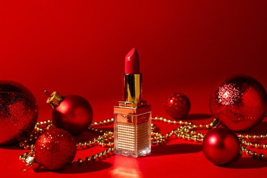 Photo of Christmas gift. Lipstick and festive decor on red background