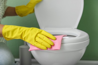 Photo of Woman cleaning toilet seat in restroom, closeup