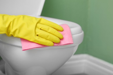 Photo of Woman cleaning toilet seat in restroom, closeup