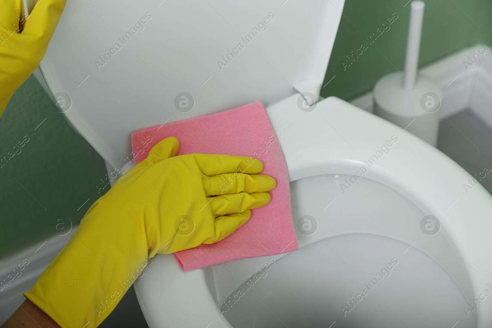 Photo of Woman cleaning toilet seat in restroom, closeup