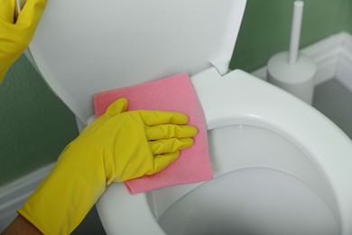 Photo of Woman cleaning toilet seat in restroom, closeup