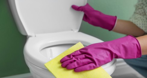 Photo of Woman cleaning toilet seat in restroom, closeup