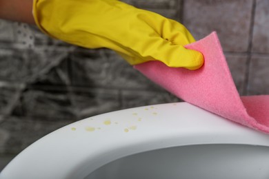 Photo of Woman wiping urine drops from toilet seat in restroom, closeup