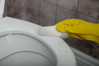 Photo of Woman wiping urine drops from toilet seat in restroom, closeup