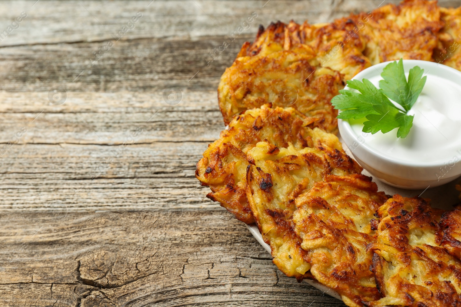 Photo of Delicious potato pancakes, sour cream and parsley on wooden table, closeup. Space for text