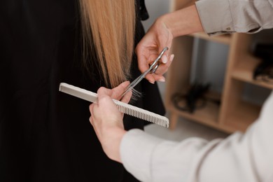 Photo of Hairdresser cutting client's hair with scissors in salon, closeup