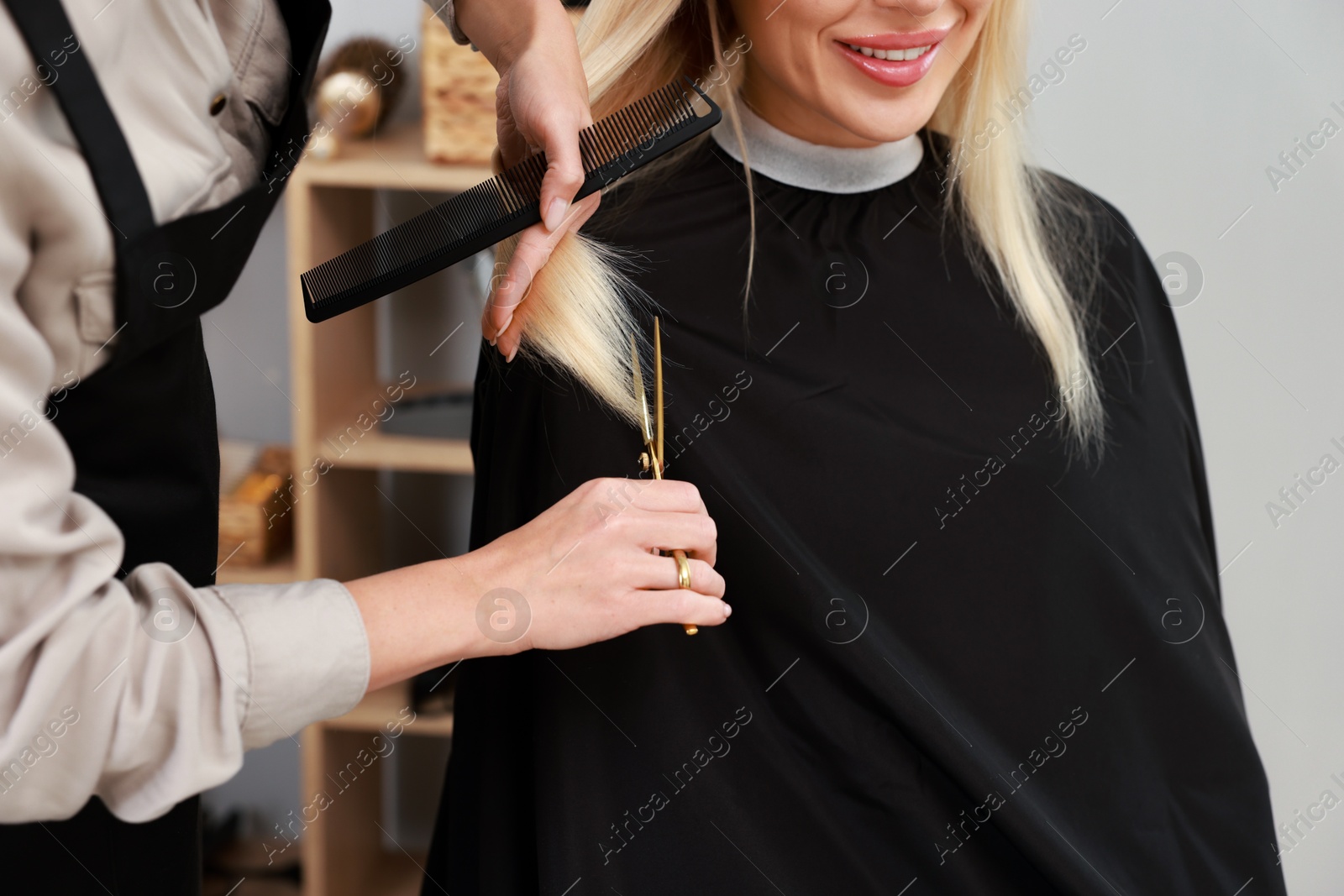 Photo of Hairdresser cutting client's hair with scissors in salon, closeup