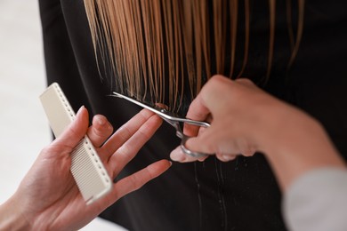 Photo of Hairdresser cutting client's hair with scissors in salon, closeup