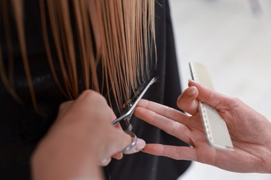 Photo of Hairdresser cutting client's hair with scissors in salon, closeup